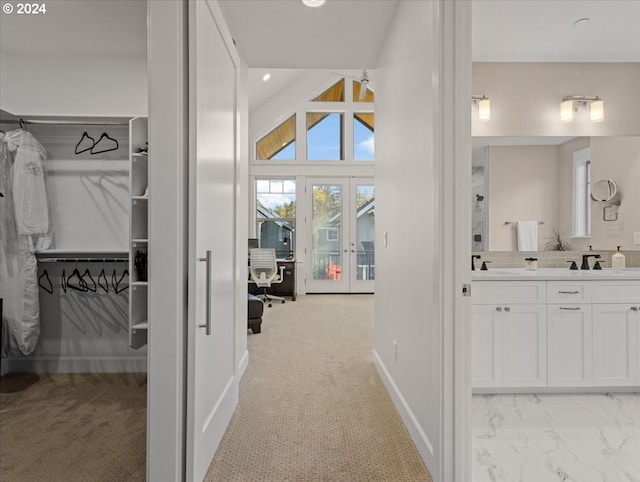 hallway with baseboards, a sink, lofted ceiling, and light colored carpet