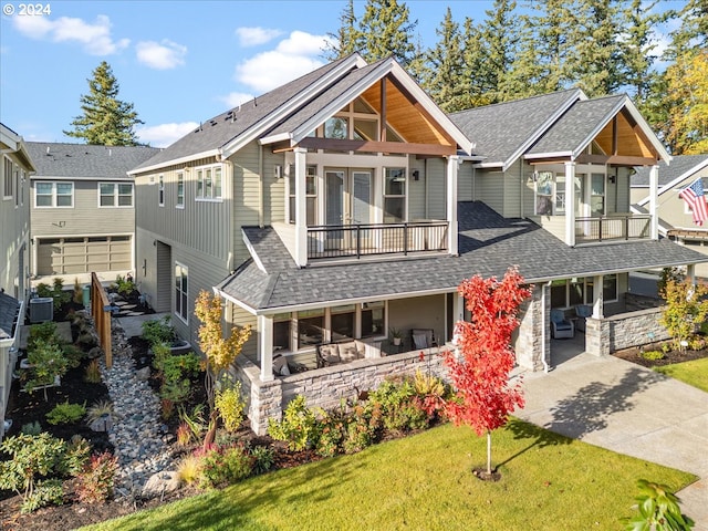 view of front of house featuring a shingled roof, a front yard, a balcony, stone siding, and driveway