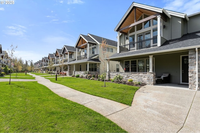 exterior space with stone siding, a front lawn, a balcony, a shingled roof, and a residential view
