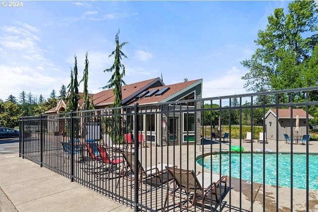 community pool with a patio area, fence, and an outdoor structure