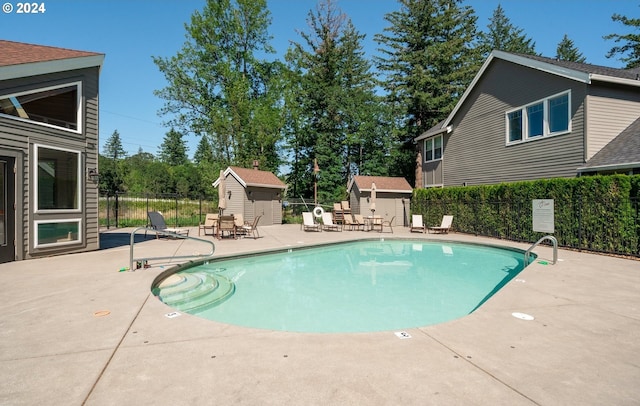 community pool with a storage shed, a patio area, fence, and an outdoor structure