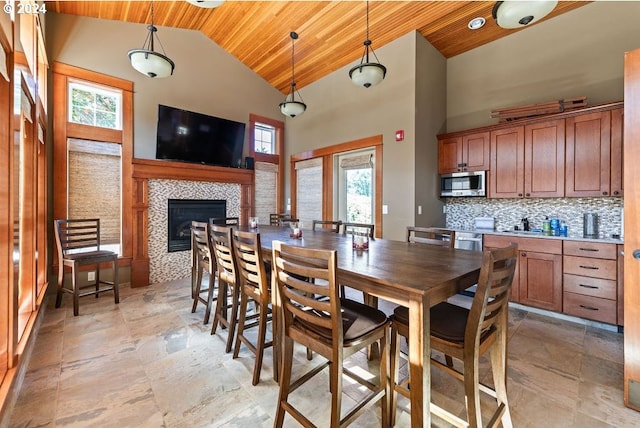 dining room featuring stone finish floor, wooden ceiling, high vaulted ceiling, and a tiled fireplace