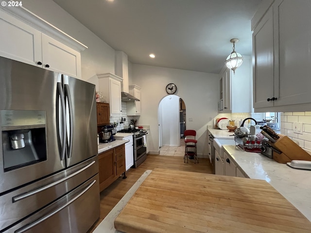 kitchen with backsplash, hanging light fixtures, white cabinetry, light hardwood / wood-style floors, and stainless steel appliances