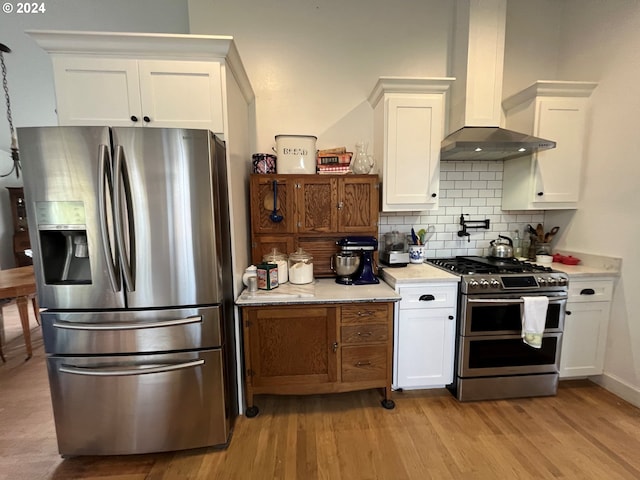 kitchen with tasteful backsplash, stainless steel appliances, wall chimney exhaust hood, white cabinets, and light hardwood / wood-style flooring