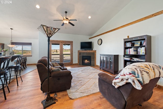 living room with ceiling fan, a tiled fireplace, vaulted ceiling, and wood-type flooring