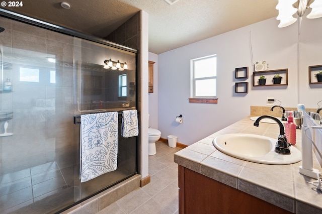 bathroom featuring toilet, tile flooring, walk in shower, vanity, and a textured ceiling