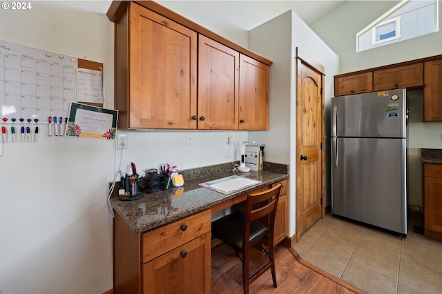 kitchen featuring dark stone counters, vaulted ceiling, stainless steel refrigerator, and light tile floors