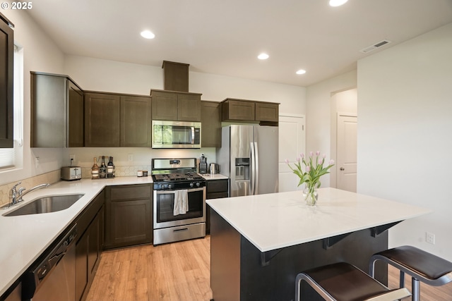 kitchen with appliances with stainless steel finishes, a sink, light wood finished floors, recessed lighting, and a kitchen bar