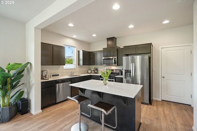 kitchen featuring appliances with stainless steel finishes, a sink, light countertops, a breakfast bar area, and light wood-style flooring