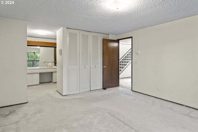 unfurnished bedroom with ensuite bathroom, light carpet, a textured ceiling, and a closet