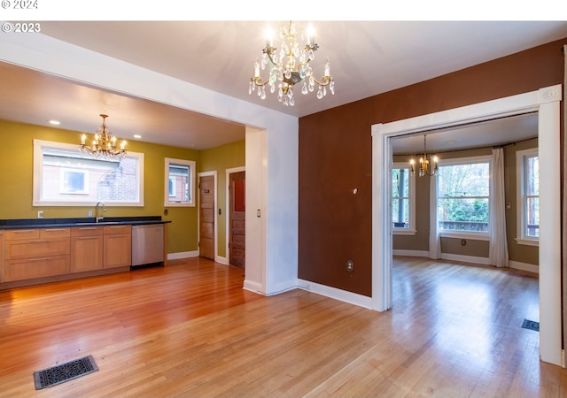 kitchen featuring stainless steel dishwasher, sink, light wood-type flooring, and decorative light fixtures