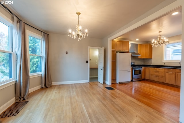 kitchen with gas range, hanging light fixtures, a wealth of natural light, wall chimney range hood, and white refrigerator