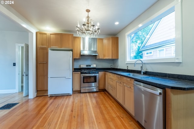 kitchen featuring a chandelier, appliances with stainless steel finishes, wall chimney exhaust hood, and light hardwood / wood-style flooring