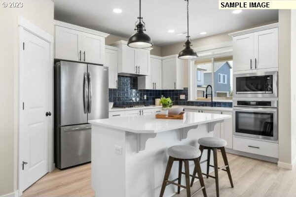 kitchen featuring white cabinets, appliances with stainless steel finishes, decorative light fixtures, and a kitchen island