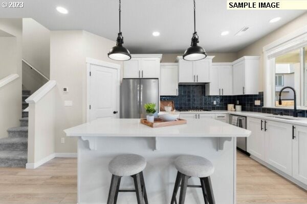 kitchen with sink, a kitchen island, pendant lighting, white cabinets, and appliances with stainless steel finishes