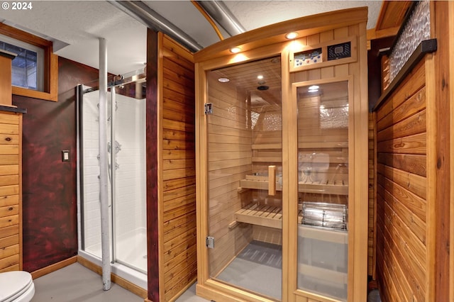 bathroom featuring toilet, wood walls, a shower with shower door, and a textured ceiling