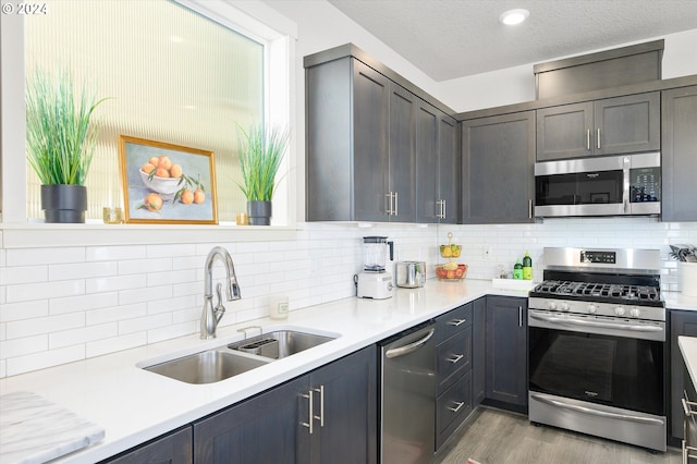 kitchen featuring sink, appliances with stainless steel finishes, backsplash, a textured ceiling, and light wood-type flooring