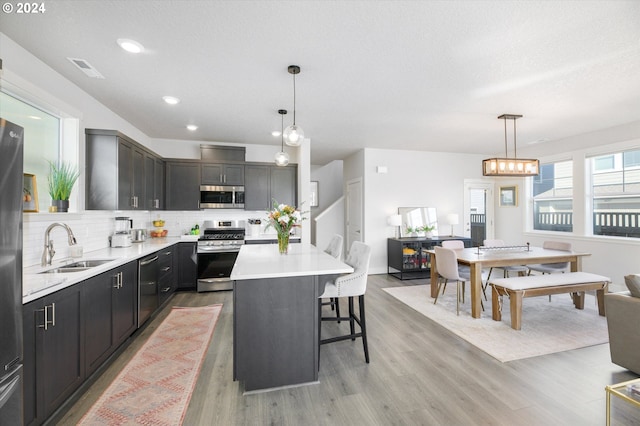 kitchen with pendant lighting, sink, appliances with stainless steel finishes, a kitchen bar, and a kitchen island