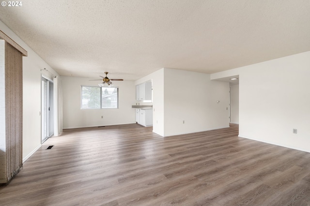 unfurnished living room featuring dark wood-type flooring, a textured ceiling, and ceiling fan