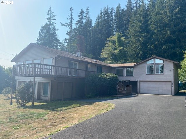 front facade with a wooden deck, a garage, and a front lawn