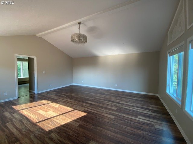 spare room featuring dark wood-type flooring, a chandelier, and vaulted ceiling with beams