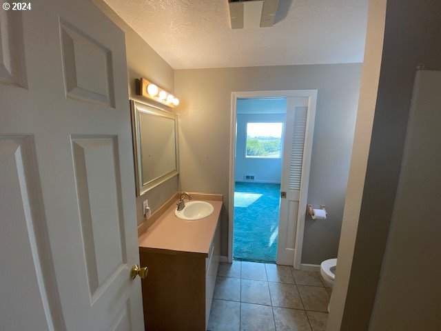 bathroom with tile patterned flooring, toilet, a textured ceiling, and vanity