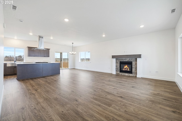 unfurnished living room with dark hardwood / wood-style flooring, a chandelier, sink, and a stone fireplace