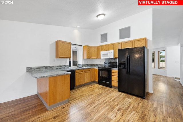 kitchen featuring black appliances, sink, light wood-type flooring, kitchen peninsula, and a high ceiling