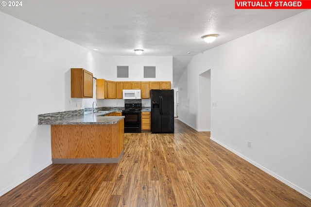 kitchen featuring black appliances, sink, a textured ceiling, kitchen peninsula, and hardwood / wood-style floors