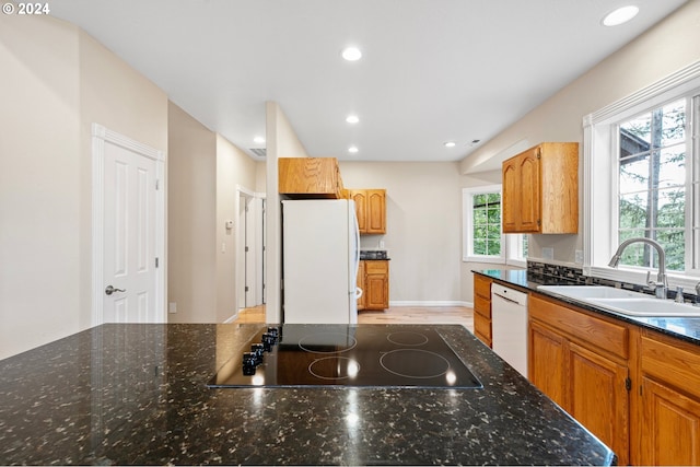 kitchen with white appliances, light hardwood / wood-style floors, dark stone counters, and sink