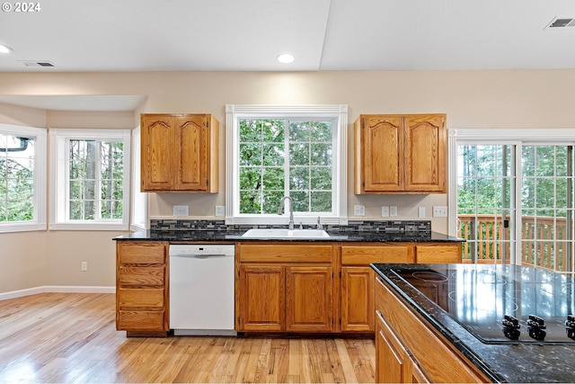 kitchen with dark stone counters, white dishwasher, sink, light hardwood / wood-style flooring, and black electric cooktop