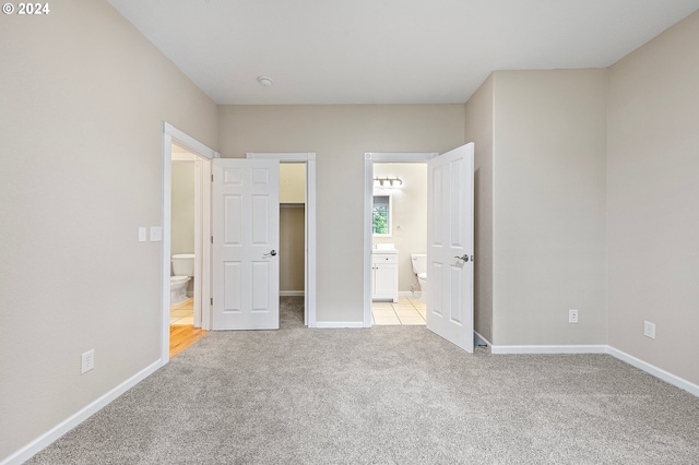 unfurnished bedroom featuring light colored carpet, a spacious closet, a closet, and ensuite bathroom