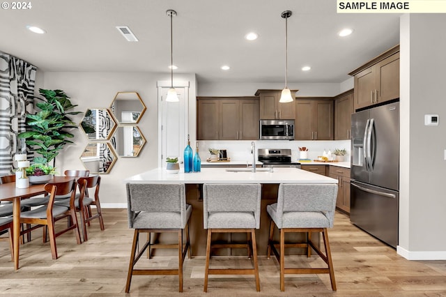 kitchen featuring light hardwood / wood-style floors, hanging light fixtures, a center island with sink, and stainless steel appliances