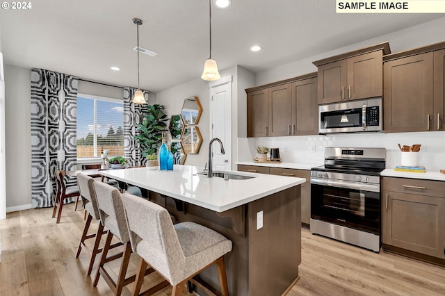 kitchen featuring sink, hanging light fixtures, stainless steel appliances, and a kitchen island with sink