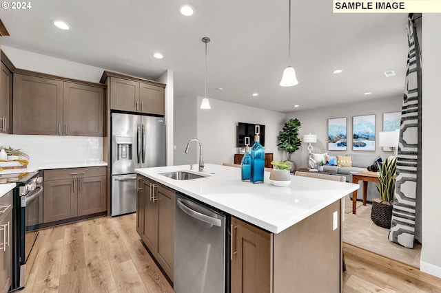 kitchen with pendant lighting, light hardwood / wood-style flooring, stainless steel appliances, sink, and a center island with sink