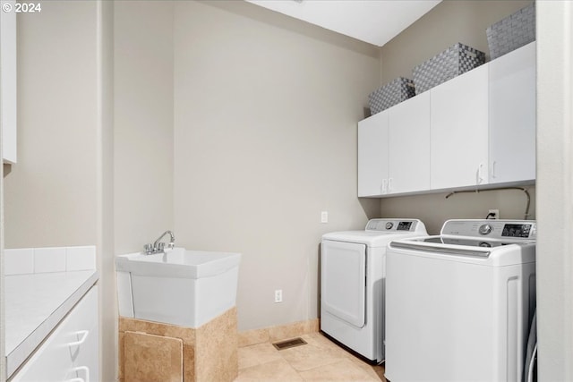 laundry area with washing machine and clothes dryer, light tile patterned floors, and cabinets