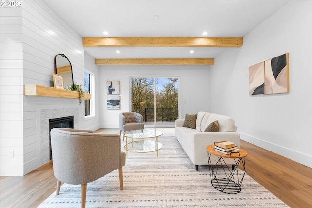 living room with beamed ceiling, a large fireplace, and light hardwood / wood-style flooring