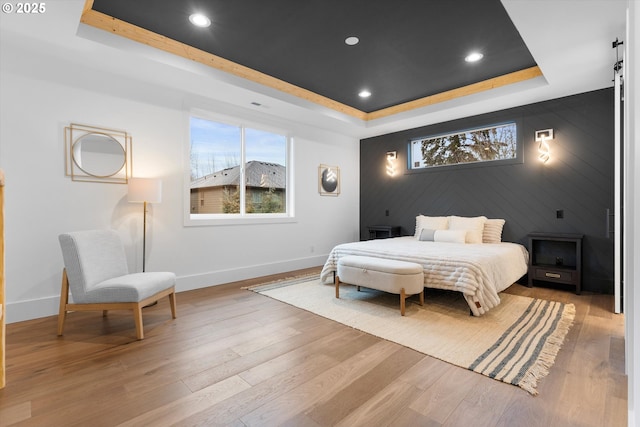 bedroom with a raised ceiling, light hardwood / wood-style floors, and multiple windows