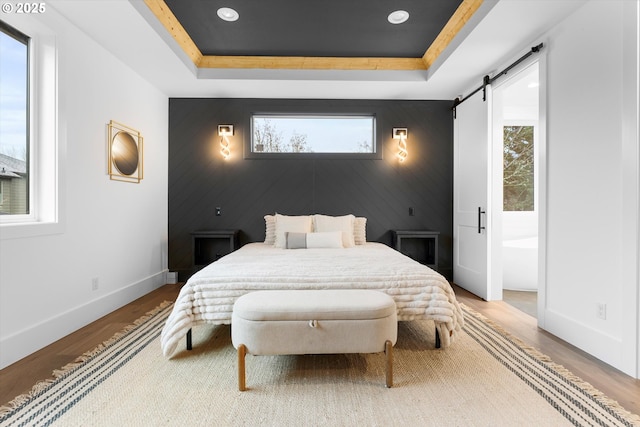 bedroom with a tray ceiling, wood-type flooring, and a barn door