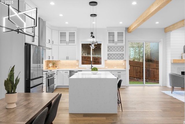 kitchen featuring appliances with stainless steel finishes, white cabinetry, a center island, light hardwood / wood-style floors, and wall chimney exhaust hood