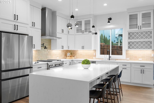 kitchen with stainless steel appliances, white cabinetry, sink, and wall chimney range hood