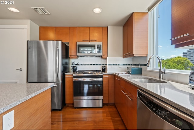 kitchen with dark hardwood / wood-style flooring, tasteful backsplash, light stone counters, stainless steel appliances, and sink