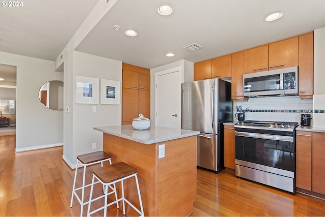 kitchen with decorative backsplash, a center island, light stone countertops, and stainless steel appliances