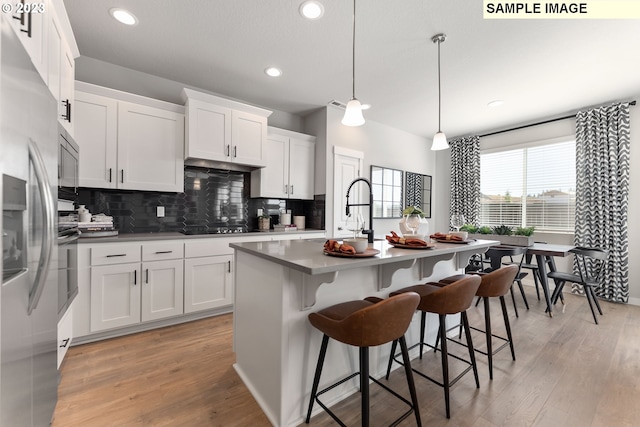 kitchen with white cabinets, a center island with sink, sink, hanging light fixtures, and light wood-type flooring