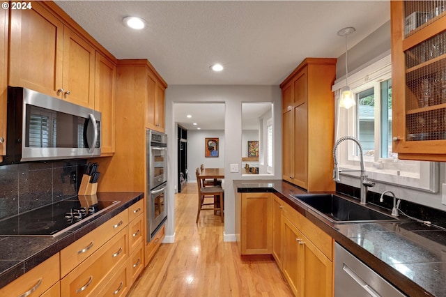 kitchen featuring appliances with stainless steel finishes, sink, light wood-type flooring, decorative light fixtures, and decorative backsplash