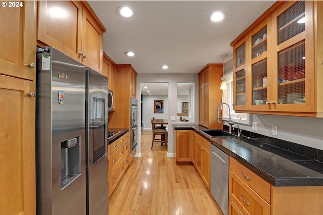 kitchen featuring hanging light fixtures, dark stone countertops, sink, appliances with stainless steel finishes, and light hardwood / wood-style floors