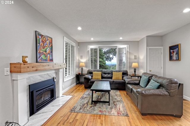 living room with a premium fireplace, a textured ceiling, and light wood-type flooring