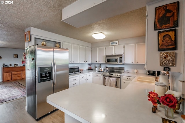 kitchen with stainless steel appliances, light hardwood / wood-style flooring, kitchen peninsula, and white cabinets