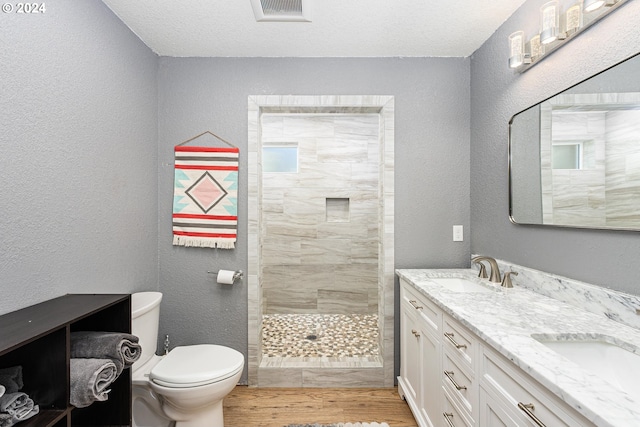 bathroom featuring double vanity, toilet, a sink, wood finished floors, and tiled shower