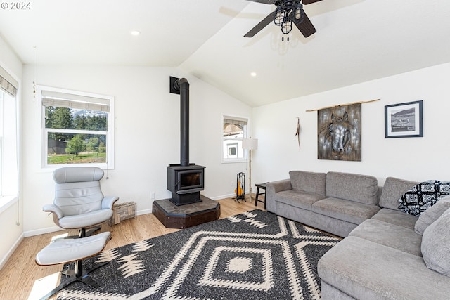 living room with lofted ceiling, ceiling fan, a wood stove, and light hardwood / wood-style flooring